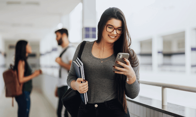 Young woman looking at her cell phone while in a university hallway