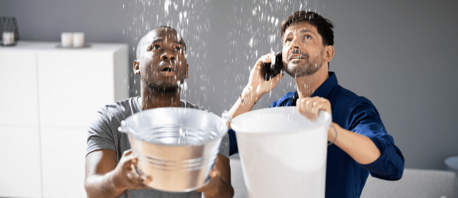 2 men holding buckets to catch rainwater from ceiling