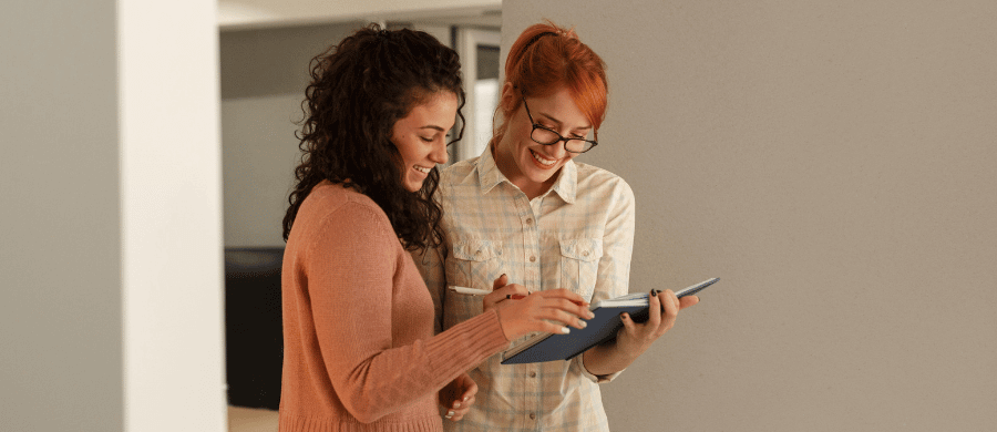 2 young women smiling and looking at notebook together