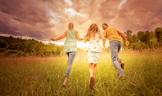 Family of three running away from the camera in an open field