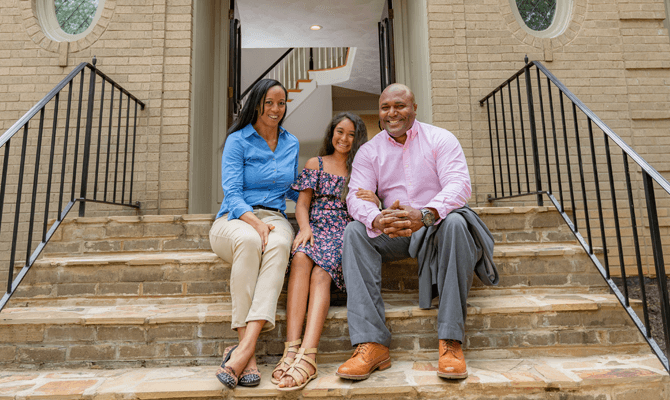 Smiling mother, father and daughter sitting on the front steps of their home
