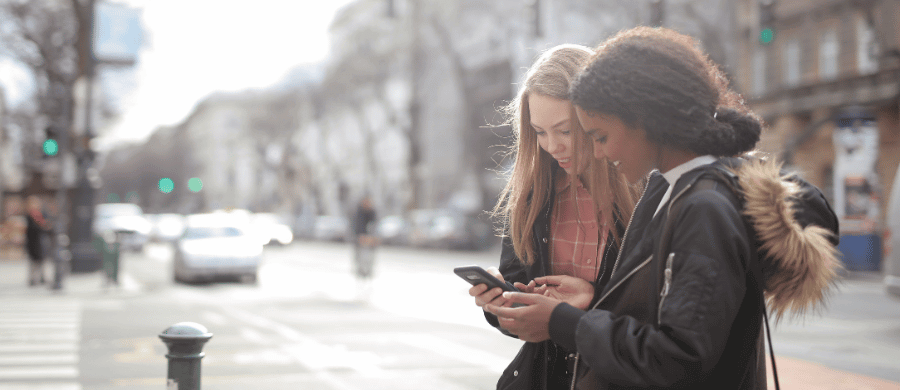 Two young women looking at a smartphone in a city