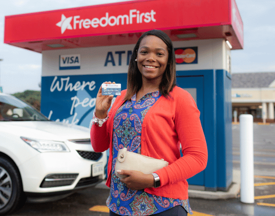 smiling woman holding debit card in front of Freedom First ATM