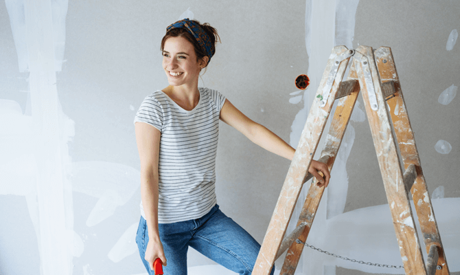 Young woman standing next to a ladder patching drywall