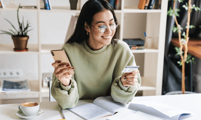 Smiling woman with smartphone in one hand and credit card in another