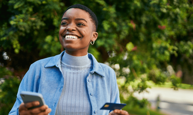 Smiling woman outside holding smartphone and credit card