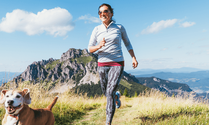 Smiling woman jogging on a mountaintop with her dog