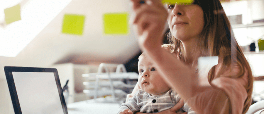 Young mother holding infant at computer and working