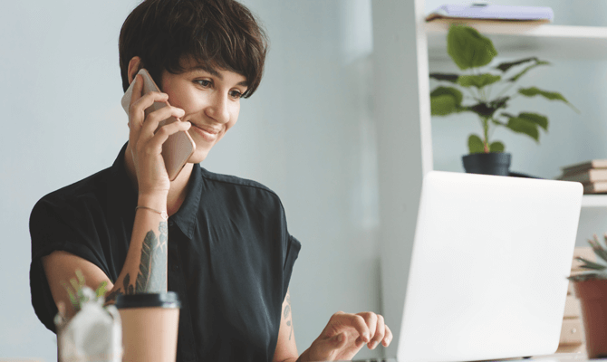 Smiling woman looking at laptop while talking on smartphone