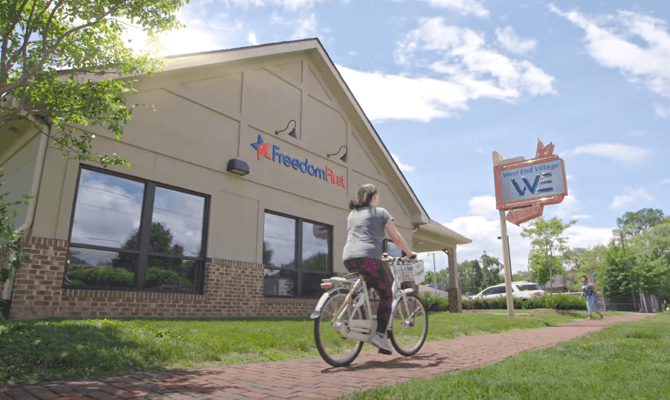 Young woman riding bicycle past Freedom First's West End branch