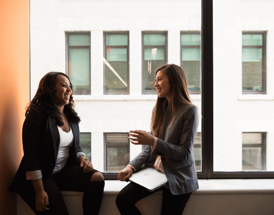 Two professional women chatting near an office window