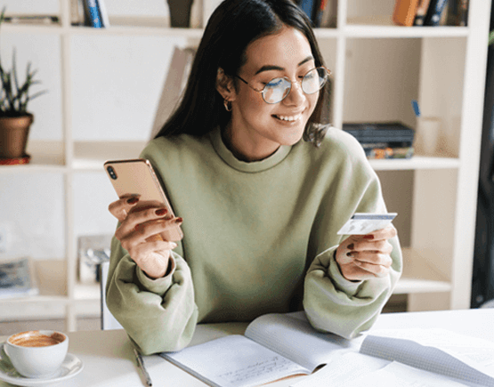 Smiling woman holding smartphone and looking at her credit card