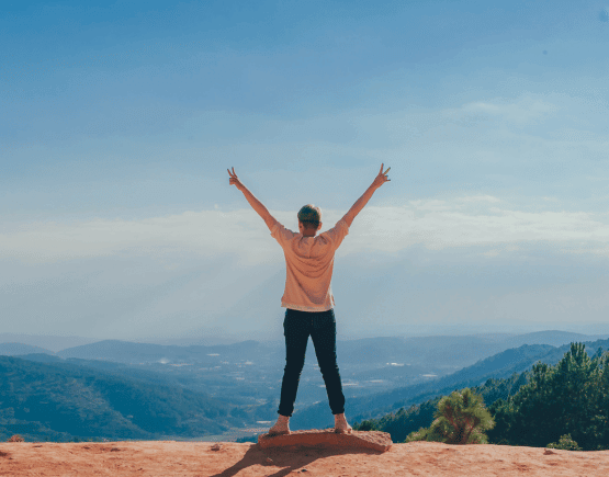 Person standing on mountain ledge with arms raised