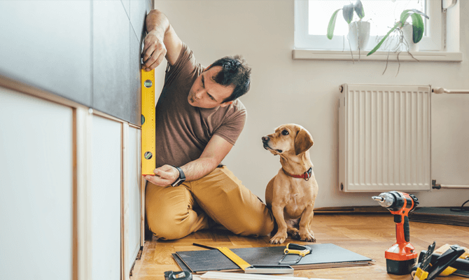 Man measuring cabinet while dog watches him