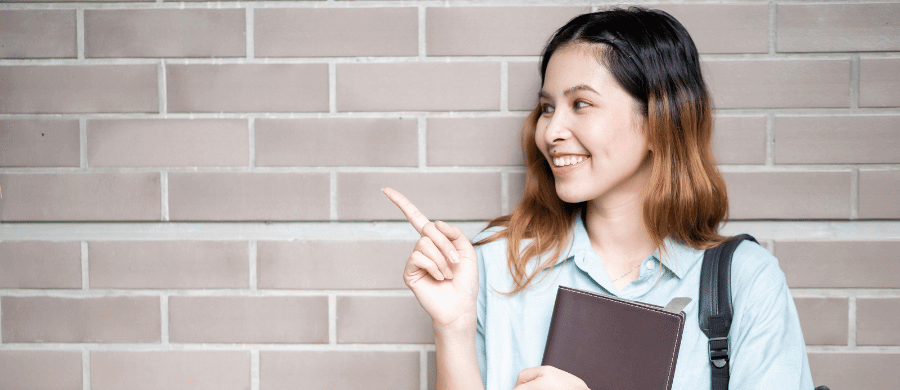 Young woman holding book and pointing to her right